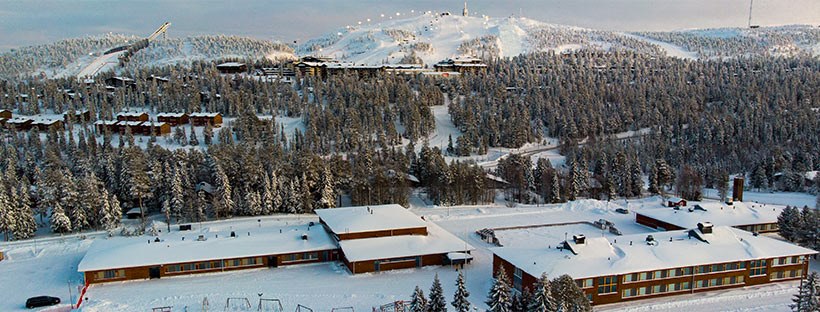 Ruka School is located right at the foot of Rukatunturi. There is a snowy landscape and a school in this picture. In the background, the lights on the ski lifts.