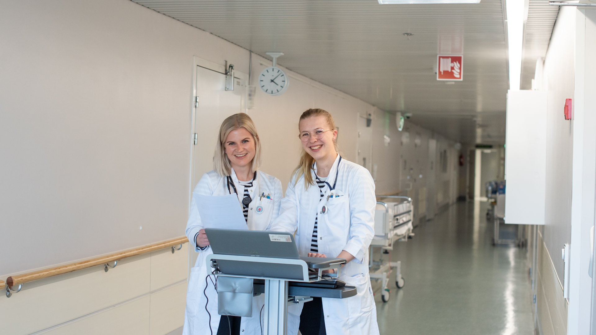 Kaksi naislääkäriä hymyilee terveyskeskuksen käytävällä