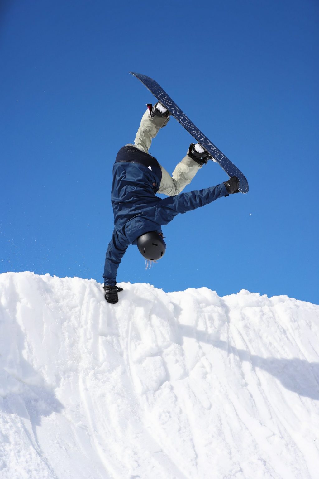 Enni Rukajärvi jumps and grabs the edge of the half-pipe and her board with one hand. There's a blue sky in the background.