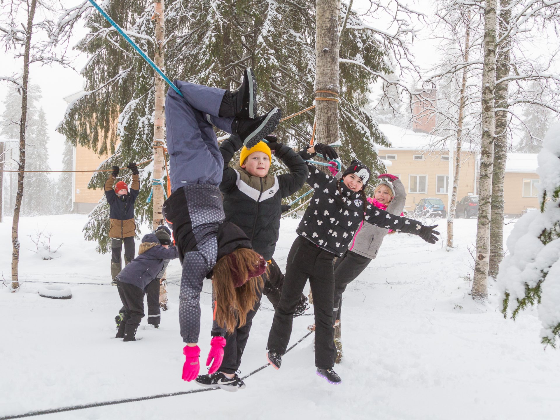 Noukavaaran koululaiset kiipeilevät iloisesti köysiradalla lumisen koulun pihametsikössä.