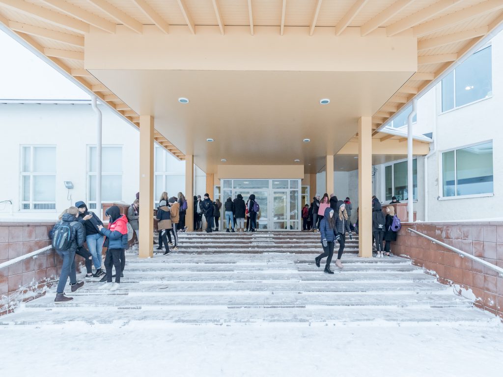 Nilon yläkoulun vaalean keltaisella katoksella varustettu pääsisäänkäynti ja oppilaita ruokavälitunnilla sen alla.