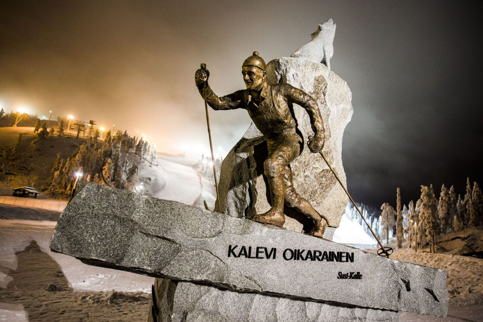 Kuvassa pronssinen Susi Kalle -patsas, jossa Kalevi Oikairainen hiihtää suden ulvoessa kivenlohkareen päällä taustalla. Lohkareesta kohoaa Suomen muoto.